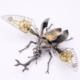 A steampunk beetle sculpture made from metallic parts, featuring silver and black steel elements, gold gears, and clear wing structures, photographed on a clean white background.